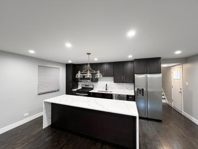 kitchen with dark hardwood / wood-style flooring, stainless steel appliances, sink, decorative light fixtures, and a kitchen island