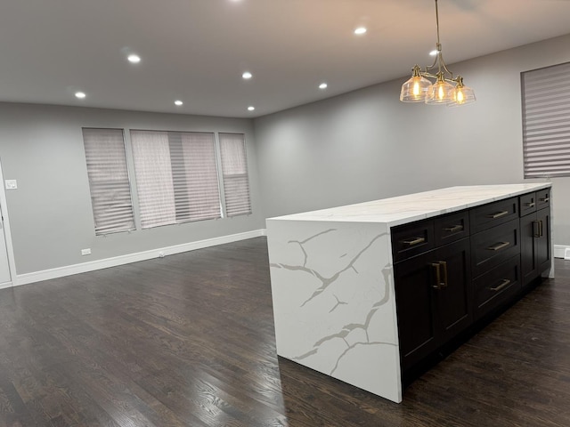 kitchen featuring a center island, dark wood-type flooring, an inviting chandelier, hanging light fixtures, and light stone counters