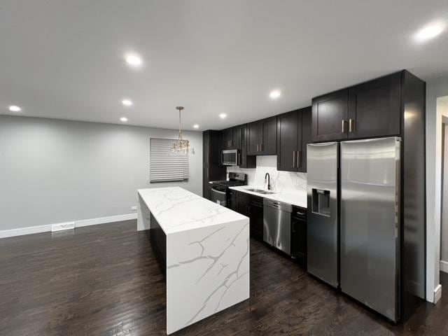 kitchen with sink, a center island, dark wood-type flooring, decorative light fixtures, and appliances with stainless steel finishes