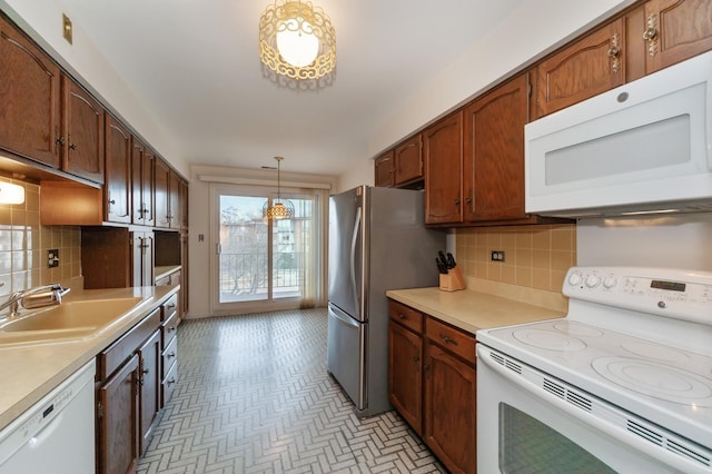 kitchen with tasteful backsplash, sink, white appliances, and decorative light fixtures