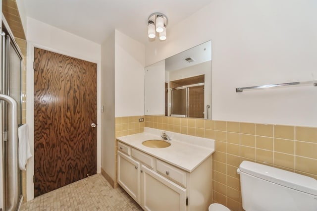 bathroom with vanity, toilet, a shower with shower door, and tile walls