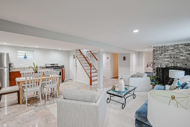 living area with a wainscoted wall, stairs, a fireplace, a decorative wall, and recessed lighting