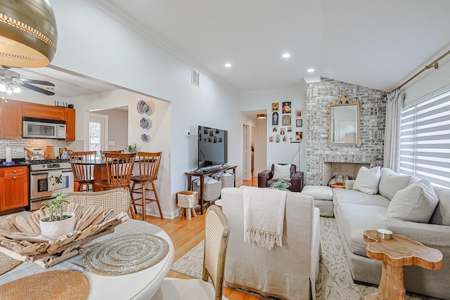 living area featuring a brick fireplace, visible vents, lofted ceiling, ornamental molding, and light wood-style floors