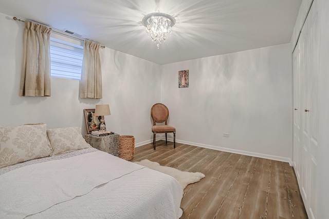 bedroom featuring a closet, visible vents, an inviting chandelier, wood finished floors, and baseboards