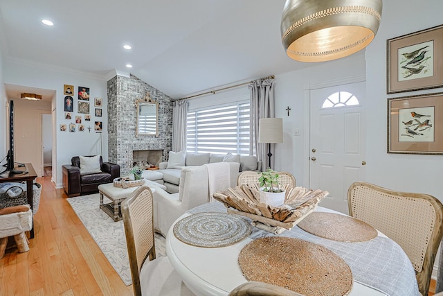 dining area featuring crown molding, a fireplace, recessed lighting, vaulted ceiling, and light wood-type flooring