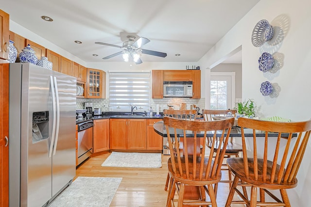 kitchen featuring dark countertops, glass insert cabinets, appliances with stainless steel finishes, brown cabinets, and a sink