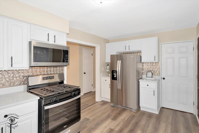 kitchen featuring stainless steel appliances, white cabinetry, light hardwood / wood-style floors, and decorative backsplash