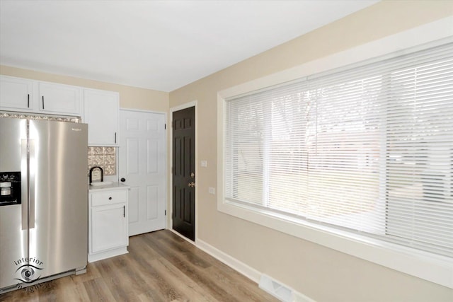 kitchen with sink, light hardwood / wood-style flooring, stainless steel fridge, white cabinets, and backsplash