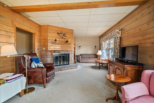 carpeted living room with wooden walls, a fireplace, and a drop ceiling