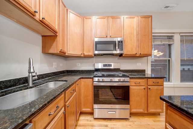 kitchen with appliances with stainless steel finishes, light hardwood / wood-style floors, sink, and dark stone counters