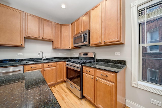 kitchen featuring light wood-type flooring, stainless steel appliances, sink, and dark stone countertops