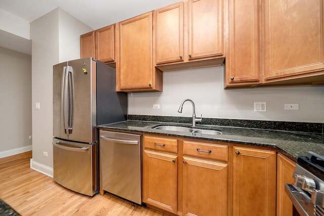 kitchen featuring sink, light hardwood / wood-style flooring, dark stone counters, and appliances with stainless steel finishes