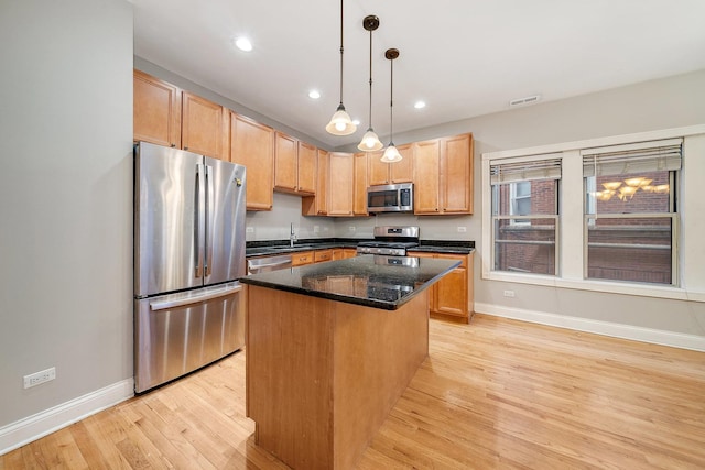 kitchen with light hardwood / wood-style flooring, dark stone countertops, hanging light fixtures, stainless steel appliances, and a kitchen island