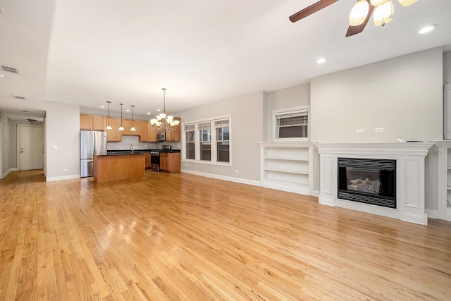 unfurnished living room featuring ceiling fan with notable chandelier, built in features, and light wood-type flooring