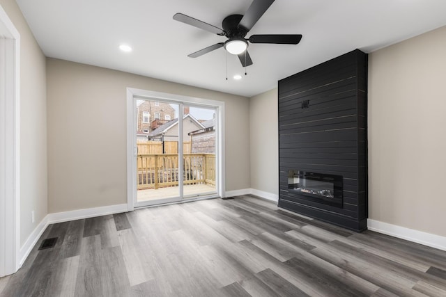 unfurnished living room featuring wood-type flooring, a large fireplace, and ceiling fan