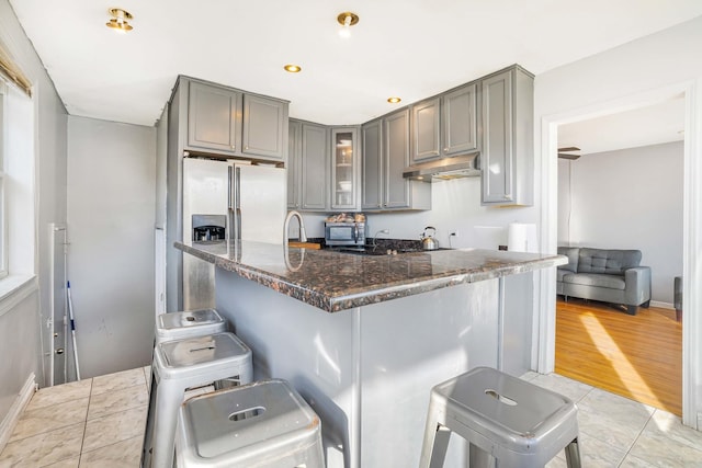 kitchen with gray cabinetry, dark stone countertops, light wood-type flooring, a kitchen bar, and kitchen peninsula