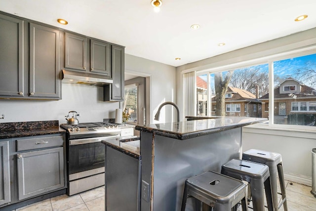 kitchen featuring a breakfast bar, light tile patterned flooring, a kitchen island with sink, dark stone counters, and gas stove