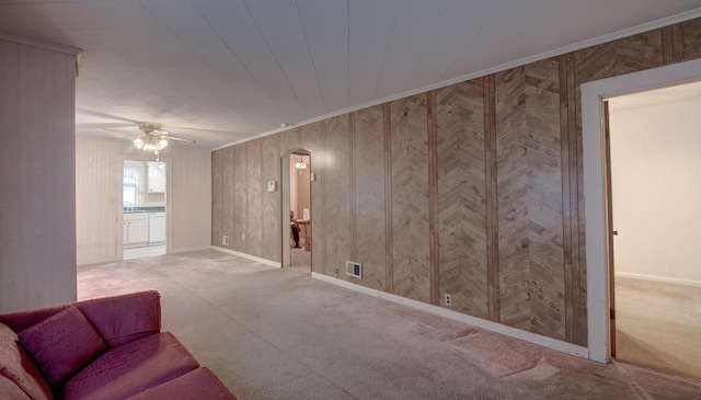 carpeted living room with ceiling fan, ornamental molding, and wooden walls