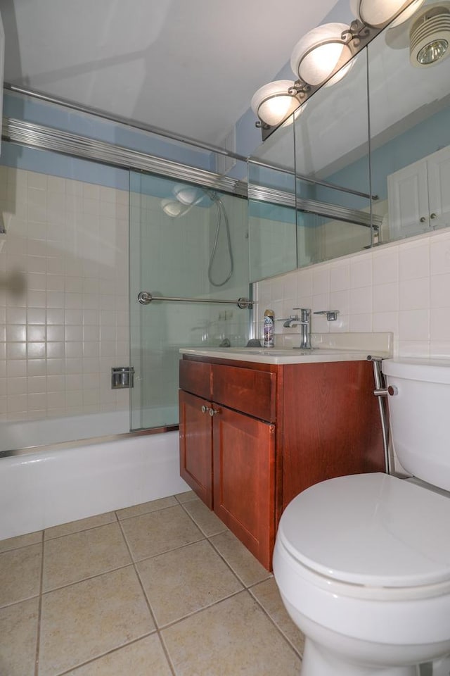 bathroom featuring tile patterned floors, toilet, vanity, combined bath / shower with glass door, and tile walls