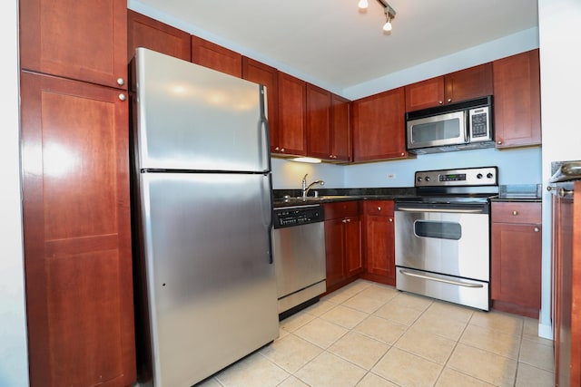 kitchen with appliances with stainless steel finishes, dark countertops, light tile patterned floors, and a sink
