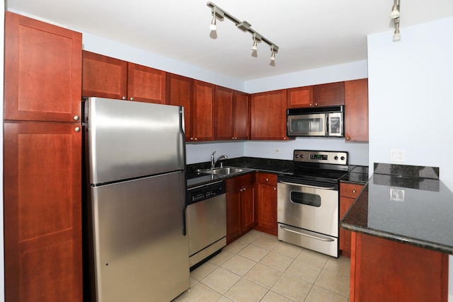 kitchen featuring appliances with stainless steel finishes, a sink, track lighting, light tile patterned floors, and dark stone counters