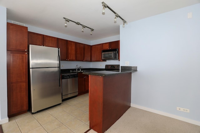 kitchen with appliances with stainless steel finishes, dark countertops, a peninsula, a sink, and baseboards