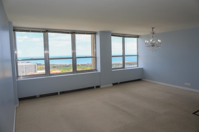 carpeted spare room featuring a chandelier, baseboards, and a water view