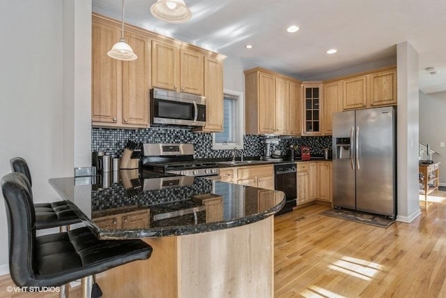 kitchen featuring kitchen peninsula, light hardwood / wood-style flooring, hanging light fixtures, stainless steel appliances, and dark stone countertops