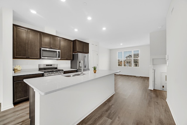 kitchen with dark brown cabinetry, sink, light hardwood / wood-style floors, a center island with sink, and appliances with stainless steel finishes