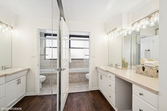 bathroom featuring wood-type flooring, tiled tub, toilet, and vanity