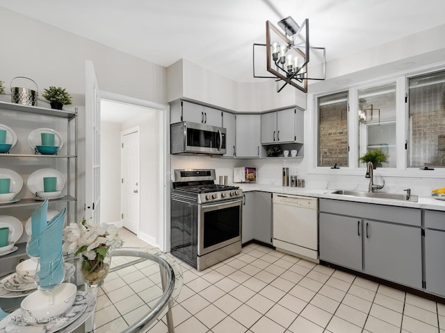 kitchen with backsplash, sink, gray cabinets, appliances with stainless steel finishes, and a chandelier