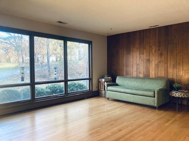 living area with light wood-type flooring, a healthy amount of sunlight, and wood walls