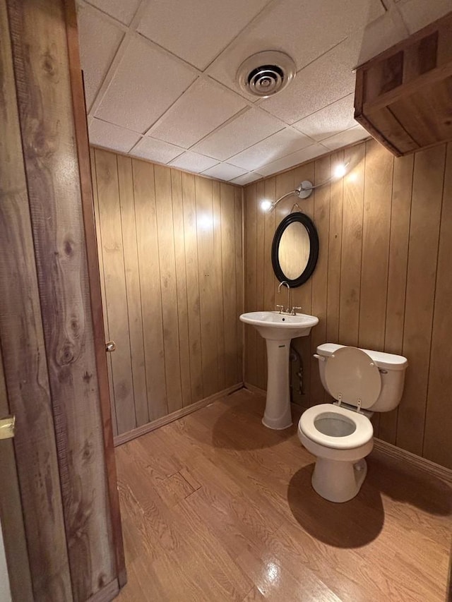 bathroom featuring hardwood / wood-style floors, a paneled ceiling, toilet, and wooden walls