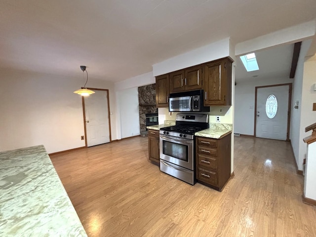 kitchen with hanging light fixtures, a skylight, light wood-type flooring, dark brown cabinetry, and stainless steel appliances