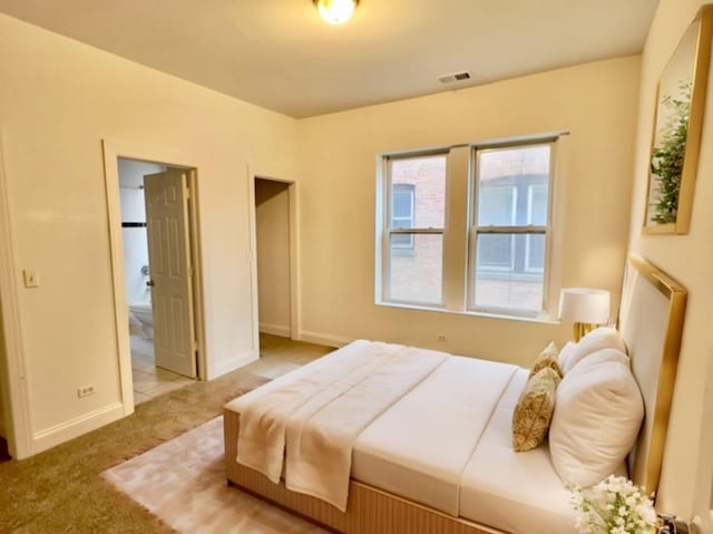 bedroom with ensuite bathroom and light colored carpet