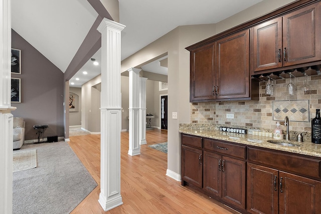 kitchen with dark brown cabinets, tasteful backsplash, ornate columns, and light stone counters