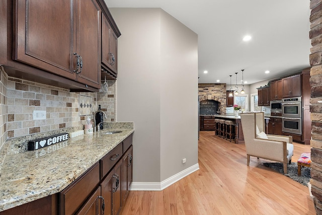 kitchen with pendant lighting, sink, light stone countertops, light hardwood / wood-style floors, and stainless steel double oven