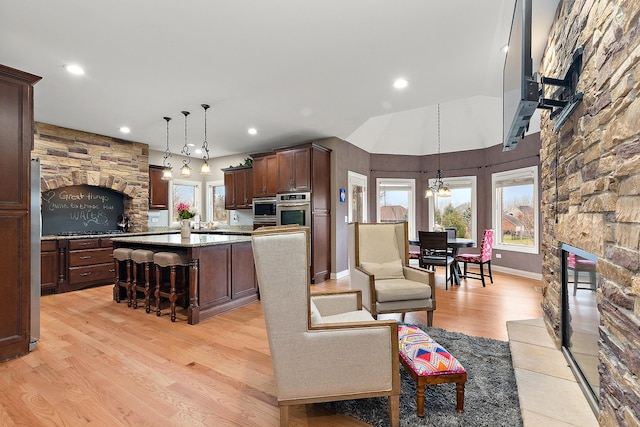 living room featuring a stone fireplace, plenty of natural light, vaulted ceiling, and light wood-type flooring