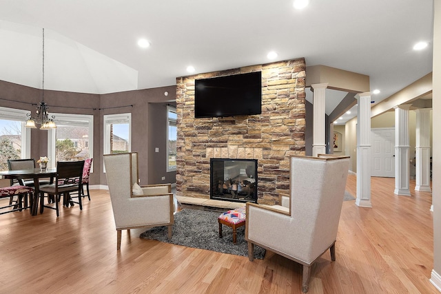 living room featuring light wood-type flooring, ornate columns, a fireplace, a chandelier, and lofted ceiling