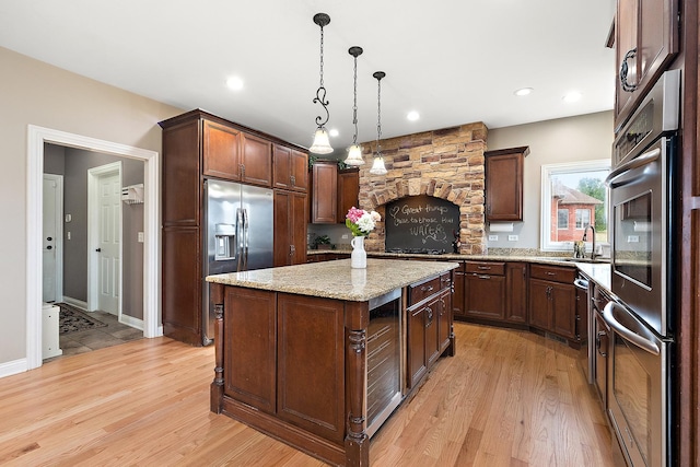 kitchen featuring pendant lighting, a center island, sink, light stone countertops, and appliances with stainless steel finishes