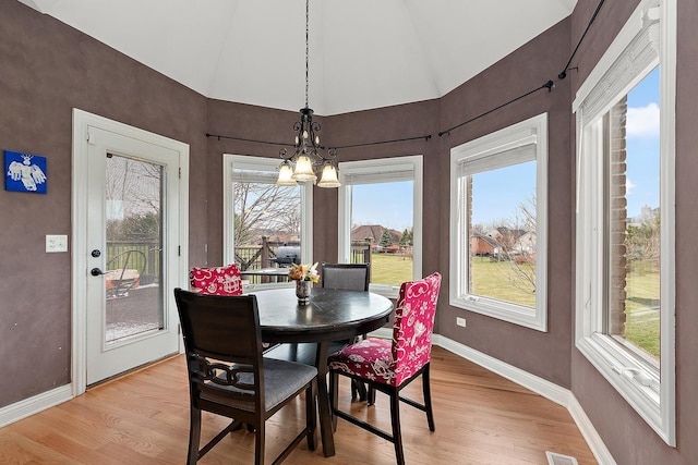 dining area with a notable chandelier, light wood-type flooring, and vaulted ceiling