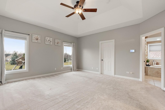 empty room with a tray ceiling, ceiling fan, and light colored carpet