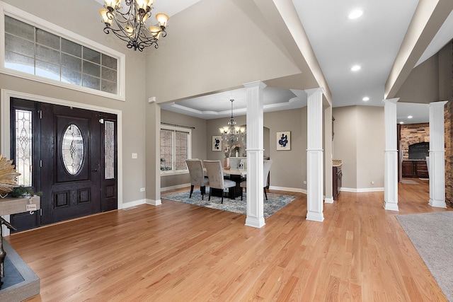 foyer featuring decorative columns, a raised ceiling, light wood-type flooring, and an inviting chandelier