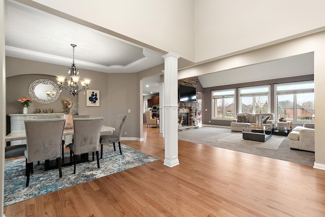 dining room with decorative columns, a raised ceiling, light hardwood / wood-style flooring, a notable chandelier, and a fireplace