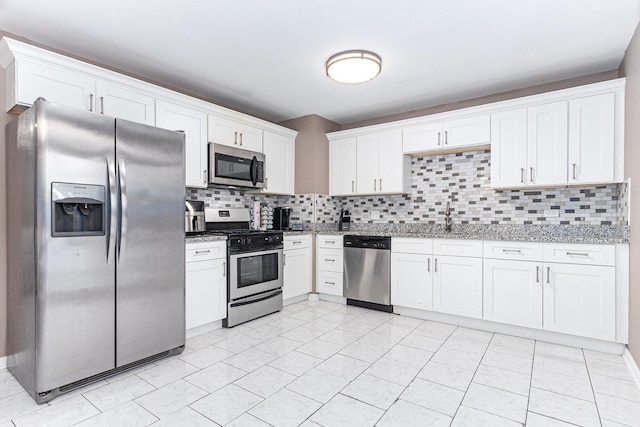 kitchen with backsplash, light stone counters, stainless steel appliances, sink, and white cabinets