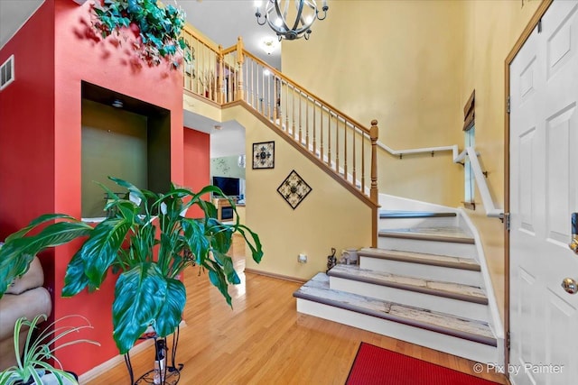 stairway featuring hardwood / wood-style flooring, a high ceiling, and a chandelier