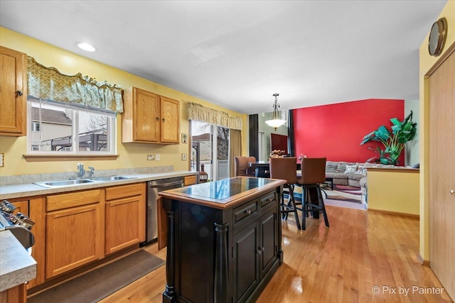 kitchen with stainless steel dishwasher, sink, light hardwood / wood-style flooring, a kitchen island, and hanging light fixtures