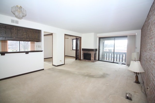 unfurnished living room featuring light carpet, a brick fireplace, a notable chandelier, and brick wall