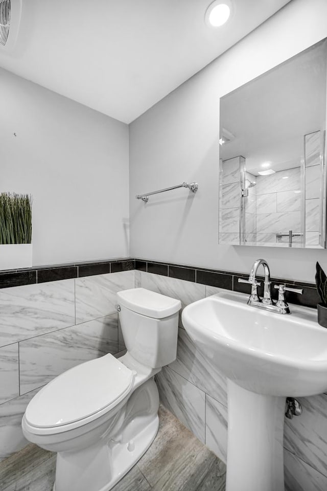 bathroom featuring wood-type flooring, toilet, and tile walls