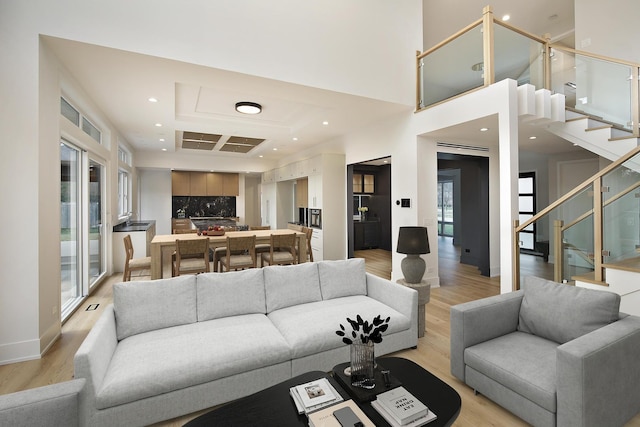 living area featuring recessed lighting, a high ceiling, baseboards, stairs, and light wood finished floors